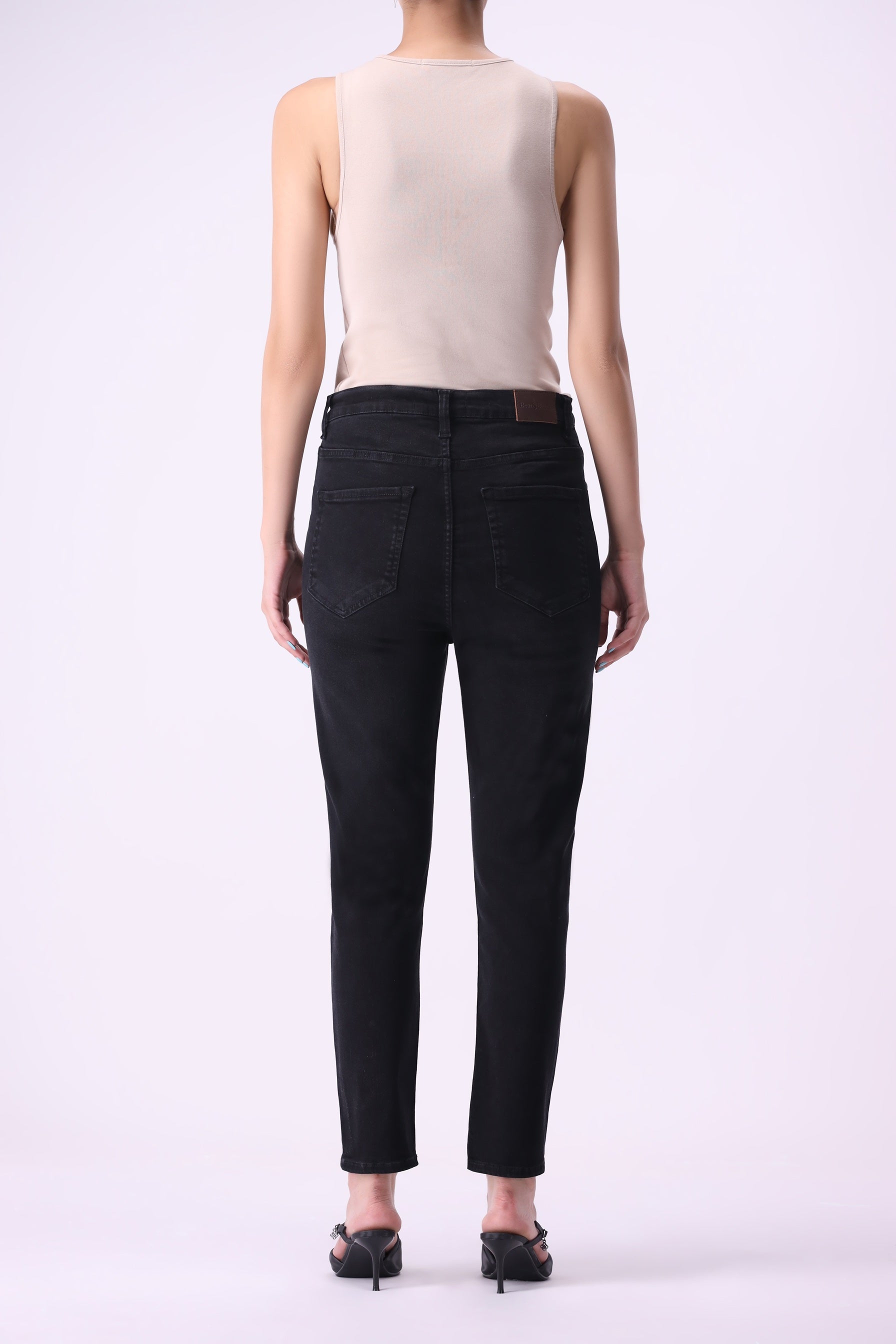 Full back view of women’s Beryoza jeans in black wash, slim tapered fit, paired with a beige tank top.