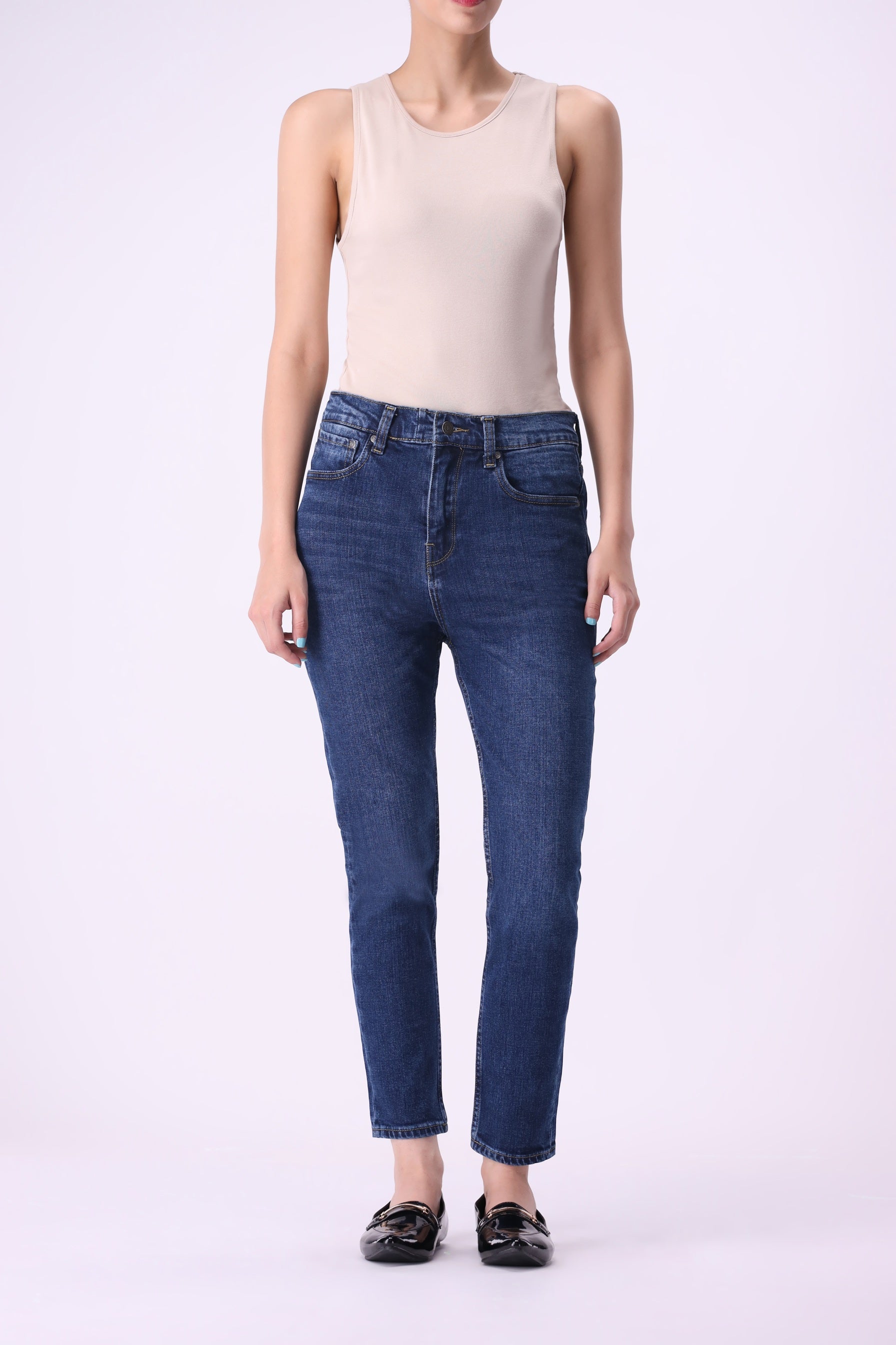 Full front view of women’s Beryoza jeans in medium dark indigo wash, slim tapered fit, paired with a beige tank top.